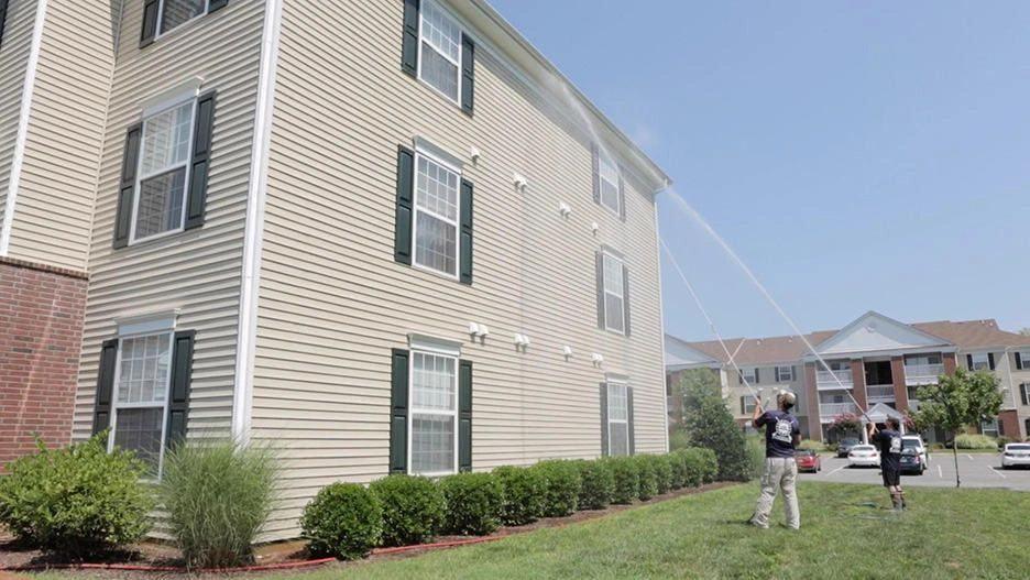 Two technicians soft washing the exterior of a multi-story apartment building