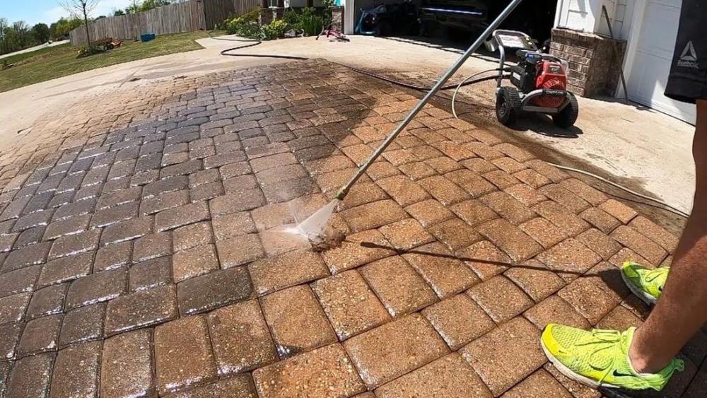 Brick paver patio being surface cleaned, clean pavers emerging beside dirty ones
